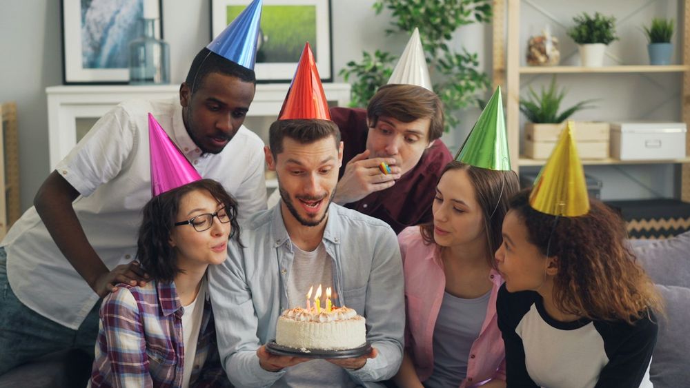Amigos con gorros de fiesta alrededor de una torta de cumpleaños con velas